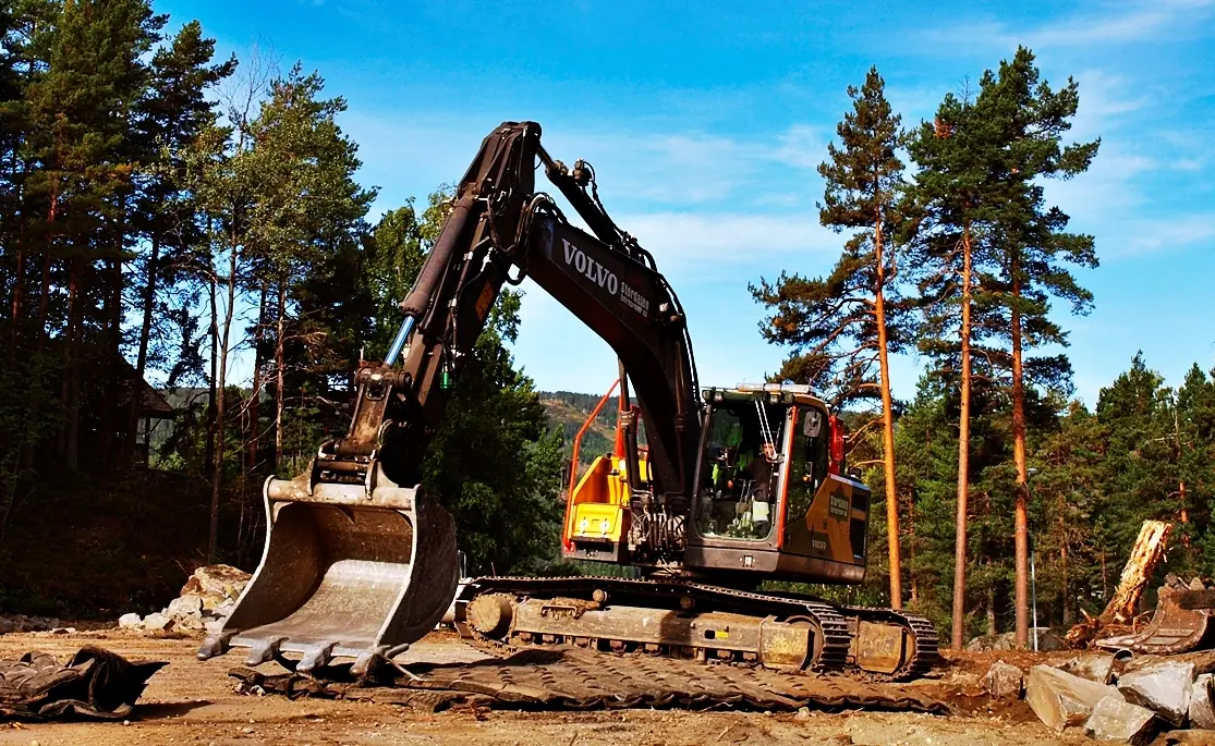 Gravemaskin blant furutrær klar for sprengning og graving