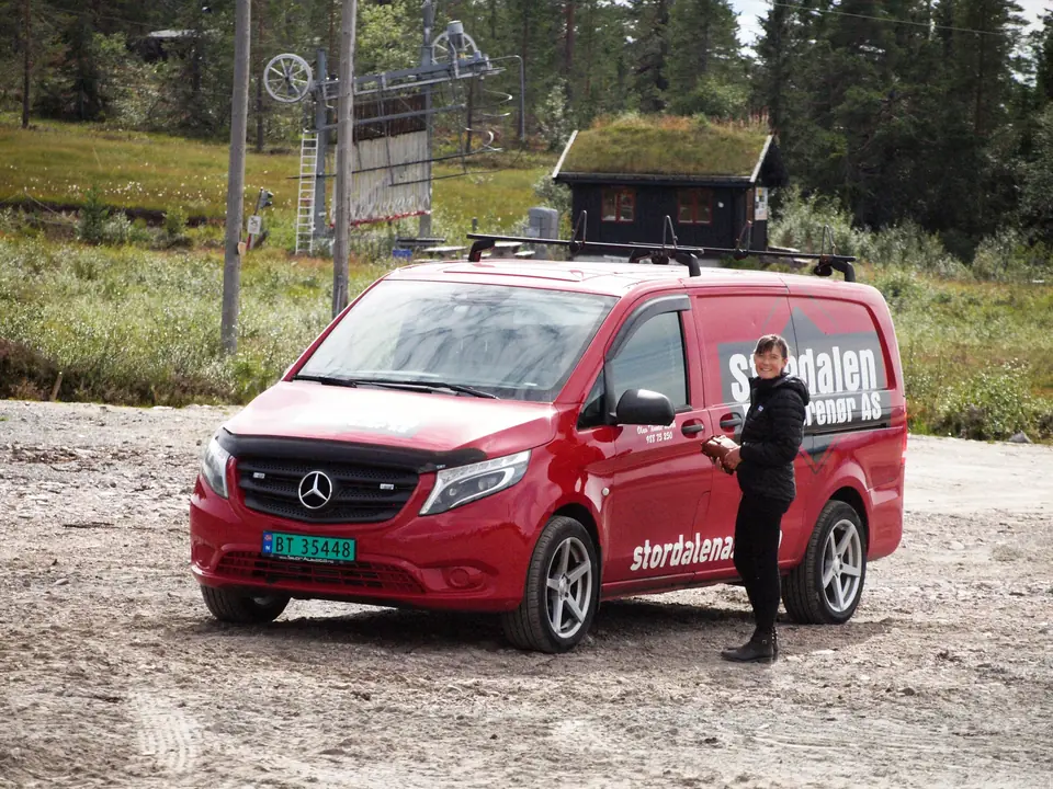 Stordalen-varebil og medarbeider ved en hyttetomt med torvtak